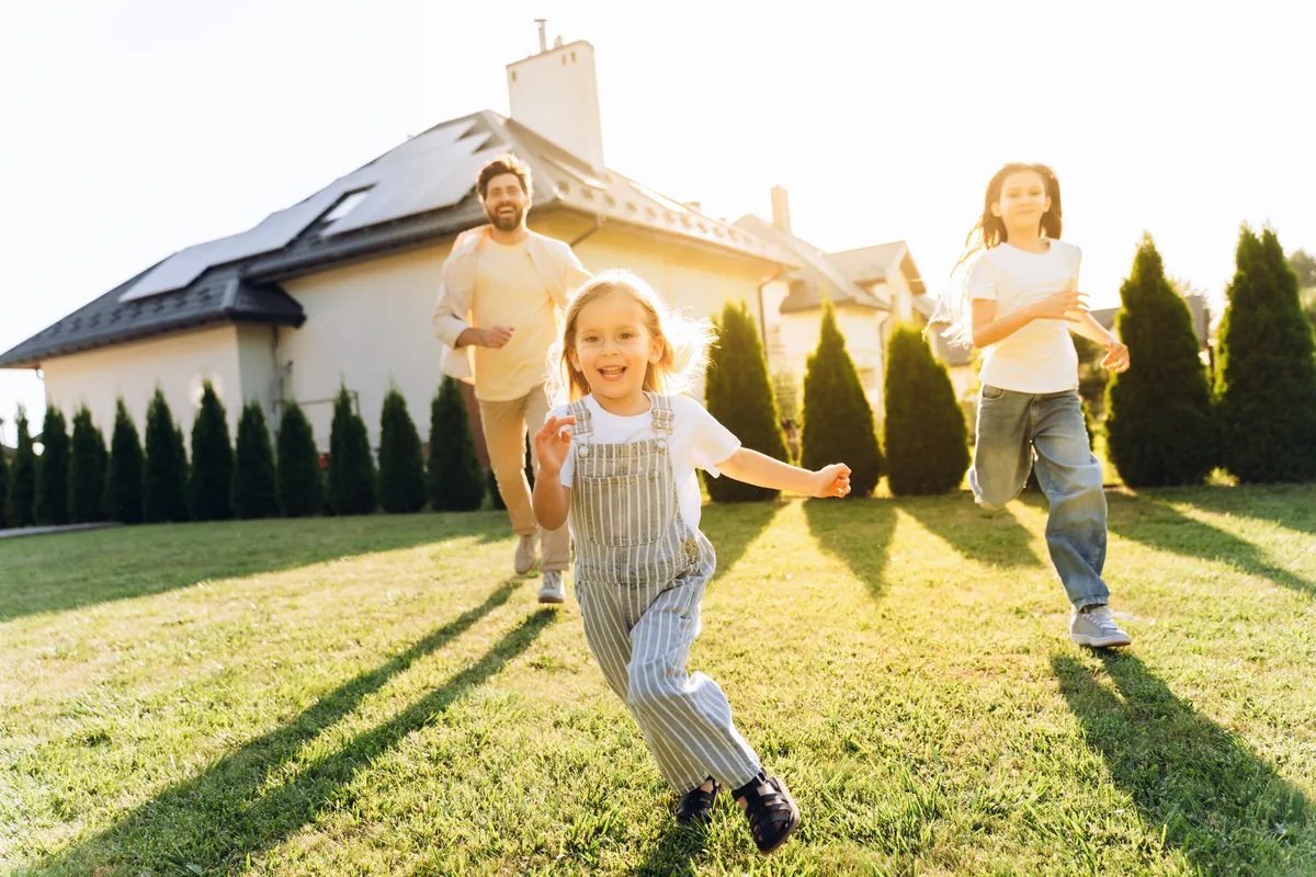 Father and two children running across a sunny lawn in front of their home