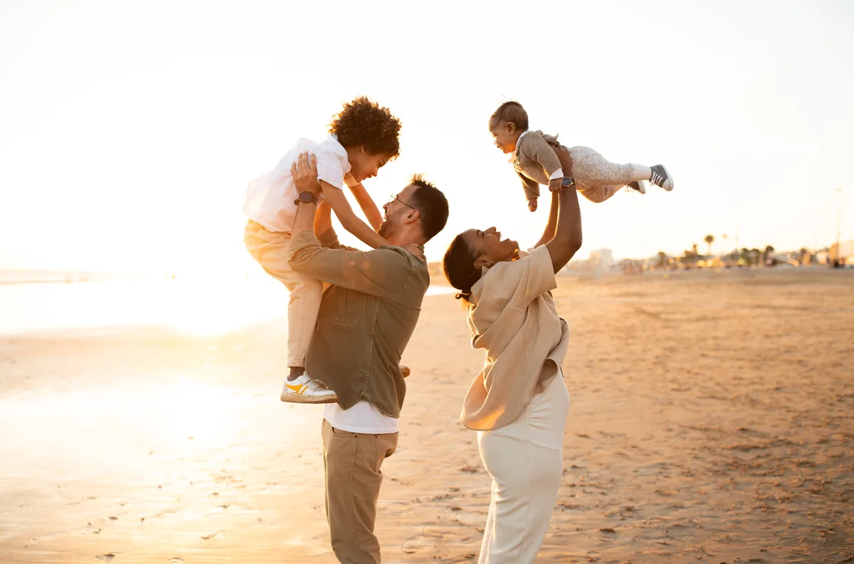 Parents lifting two children into the air on a sandy beach at sunset