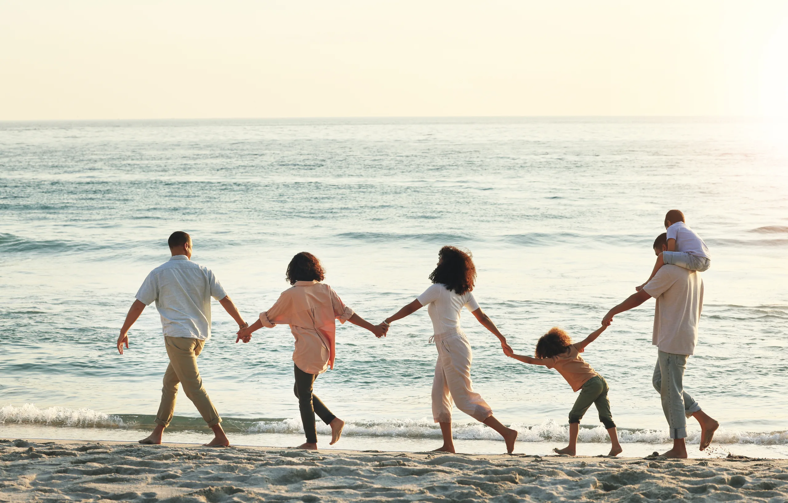 Family of five holding hands and walking along the shoreline at sunset