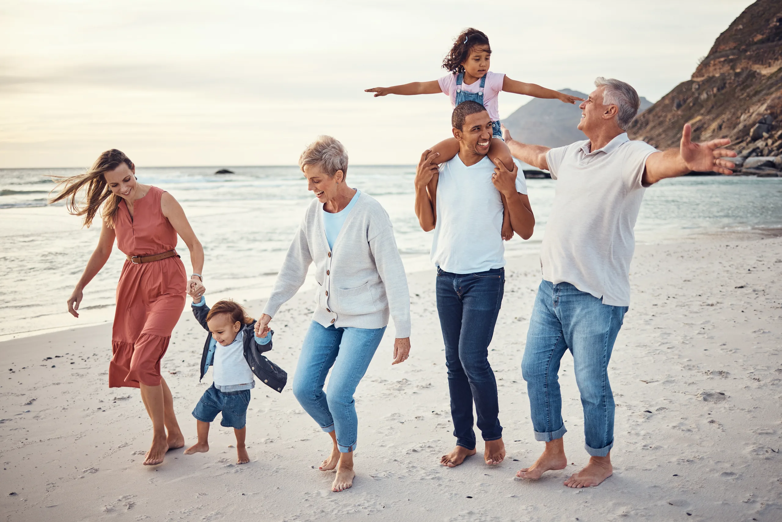 Multigenerational family walking barefoot along the beach on an overcast day
