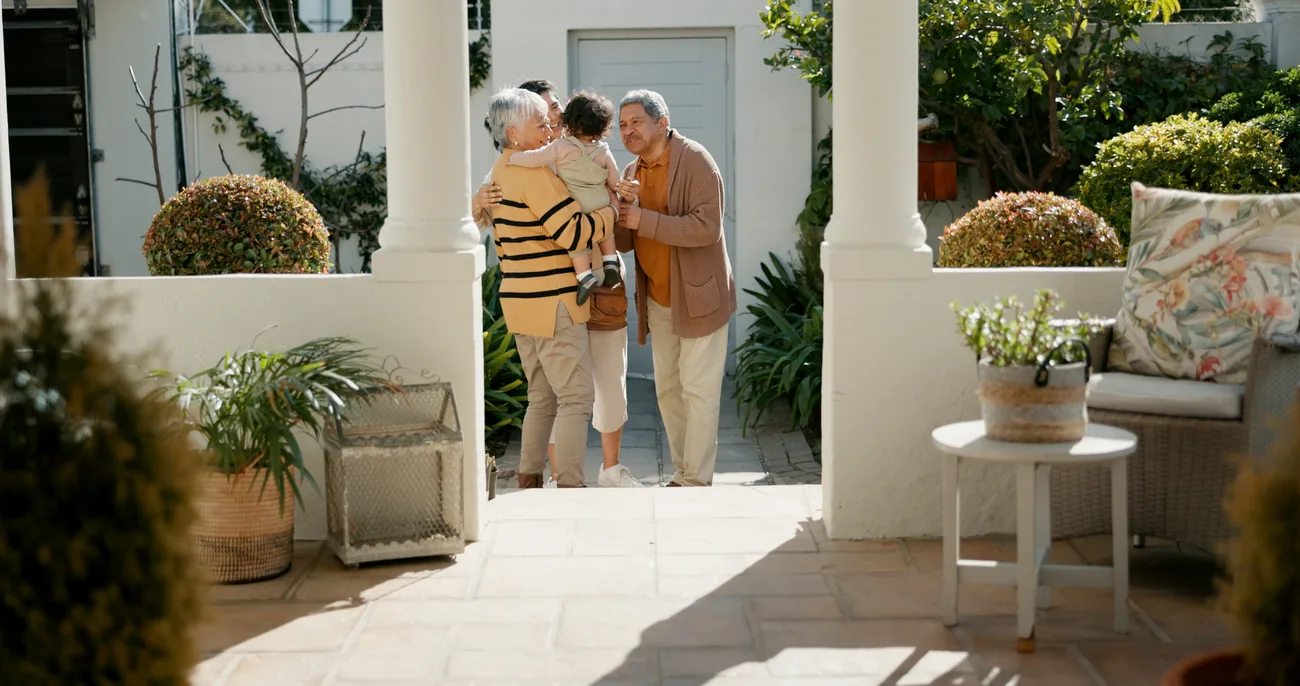 Grandparents greeting a young child on the front patio of a home