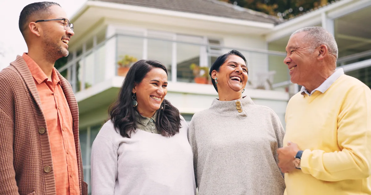 Four adults laughing together outside a home