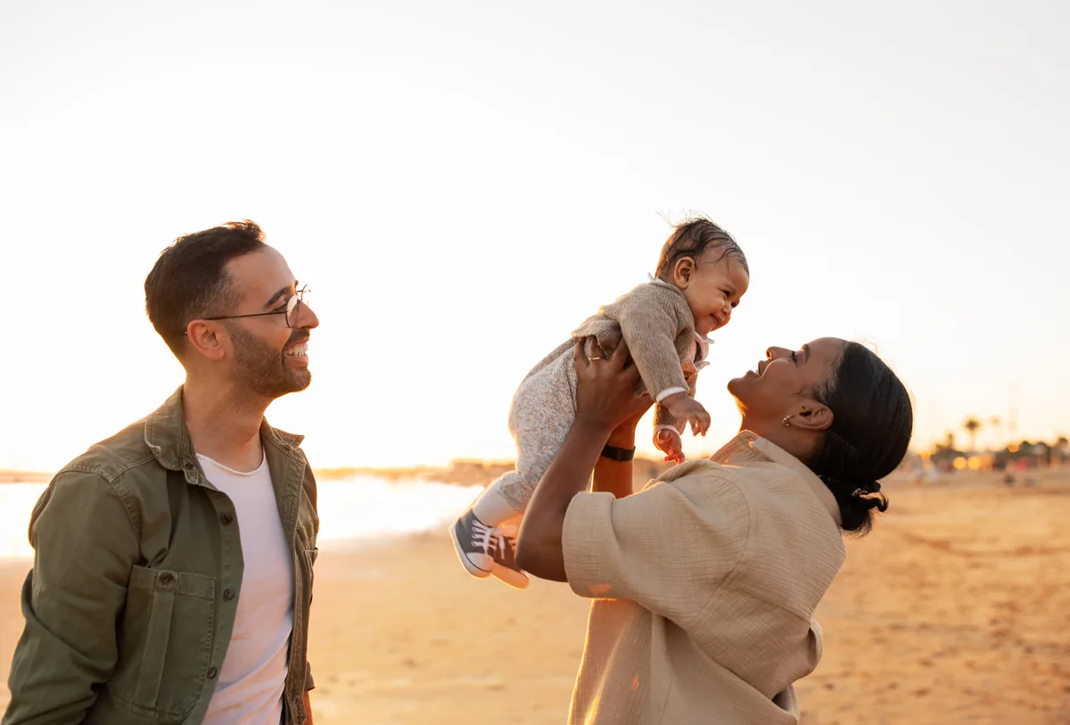 Two parents lifting their baby into the air on the beach at sunset