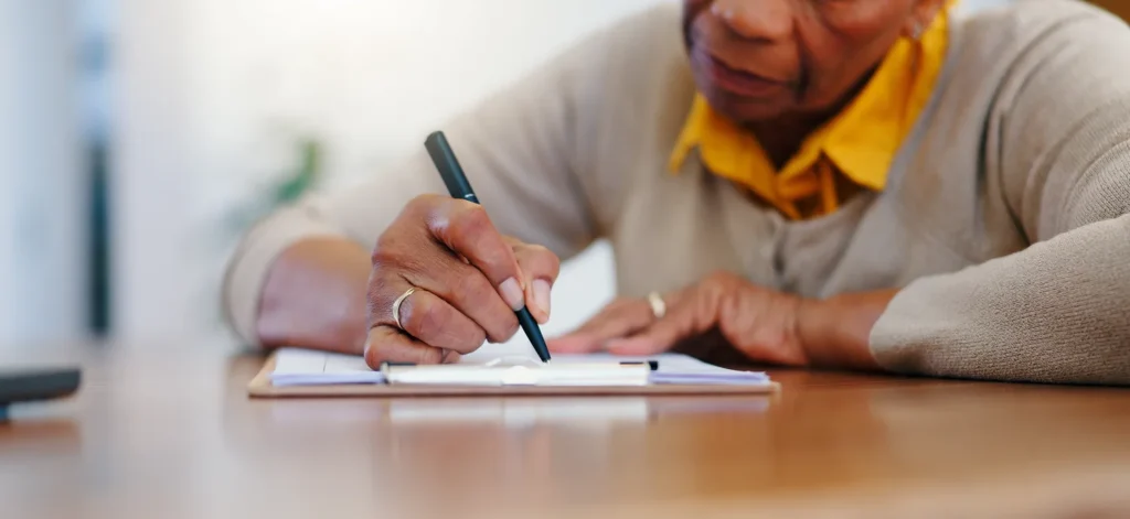 Close-up of a senior adult writing on a document with a pen