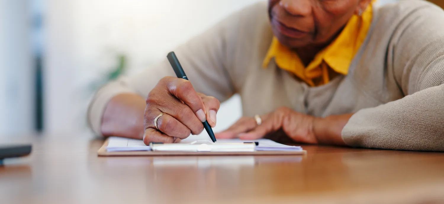 Close-up of a senior adult writing on a document with a pen