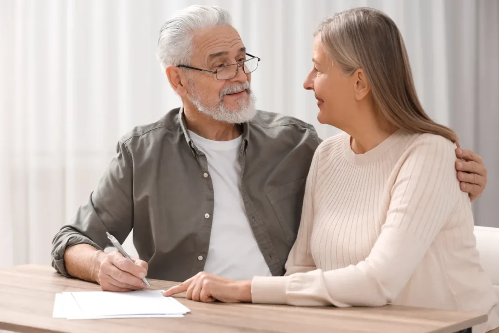 Senior couple smiling at each other while signing documents at a table