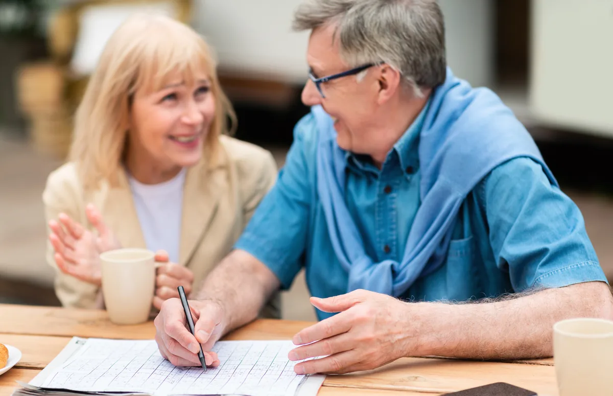 Older couple smiling over a crossword puzzle at the table