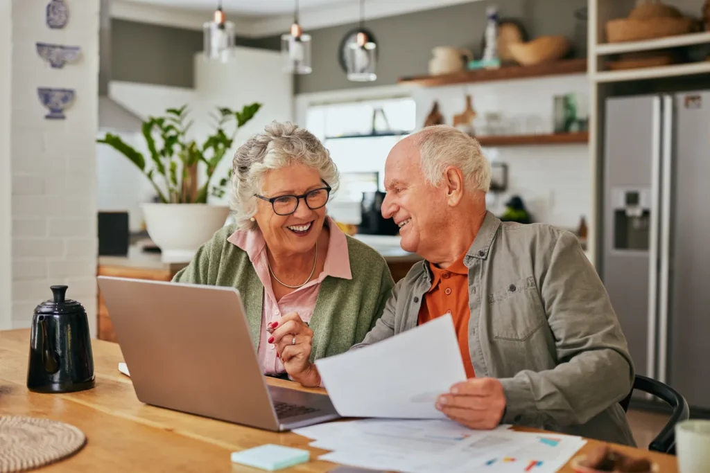 Smiling senior couple reviewing paperwork beside a laptop in their kitchen